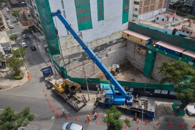Ağır vinç kazıcıyı şehir ortamında derin bir inşaat sahasına kaldırıyor, altyapı geliştirme, gayrimenkul büyümesi ve modern şehir genişlemesi sergiliyor..