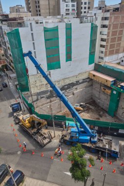 Ağır vinç kazıcıyı şehir ortamında derin bir inşaat sahasına kaldırıyor, altyapı geliştirme, gayrimenkul büyümesi ve modern şehir genişlemesi sergiliyor..