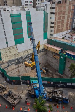 Ağır vinç kazıcıyı şehir ortamında derin bir inşaat sahasına kaldırıyor, altyapı geliştirme, gayrimenkul büyümesi ve modern şehir genişlemesi sergiliyor..