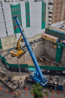 Ağır vinç kazıcıyı şehir ortamında derin bir inşaat sahasına kaldırıyor, altyapı geliştirme, gayrimenkul büyümesi ve modern şehir genişlemesi sergiliyor..