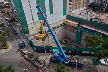 Ağır vinç kazıcıyı şehir ortamında derin bir inşaat sahasına kaldırıyor, altyapı geliştirme, gayrimenkul büyümesi ve modern şehir genişlemesi sergiliyor..