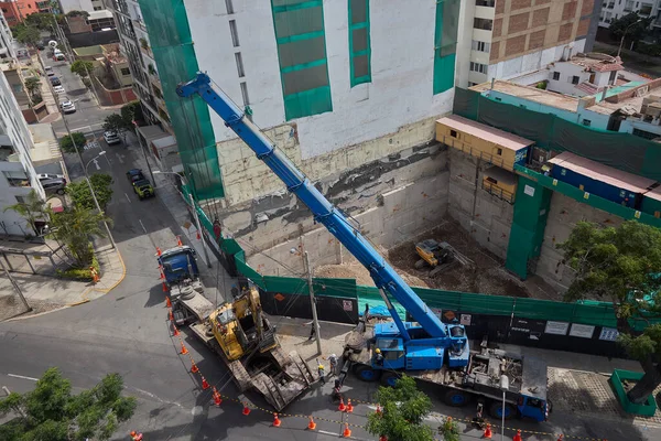 Ağır vinç kazıcıyı şehir ortamında derin bir inşaat sahasına kaldırıyor, altyapı geliştirme, gayrimenkul büyümesi ve modern şehir genişlemesi sergiliyor..
