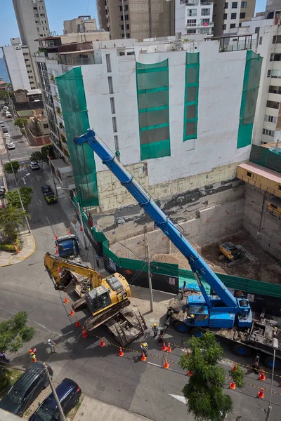 Ağır vinç kazıcıyı şehir ortamında derin bir inşaat sahasına kaldırıyor, altyapı geliştirme, gayrimenkul büyümesi ve modern şehir genişlemesi sergiliyor..