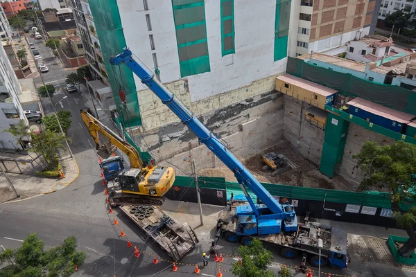 Ağır vinç kazıcıyı şehir ortamında derin bir inşaat sahasına kaldırıyor, altyapı geliştirme, gayrimenkul büyümesi ve modern şehir genişlemesi sergiliyor..