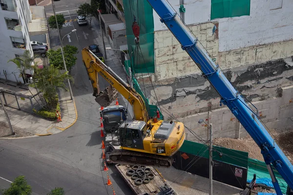 Ağır vinç kazıcıyı şehir ortamında derin bir inşaat sahasına kaldırıyor, altyapı geliştirme, gayrimenkul büyümesi ve modern şehir genişlemesi sergiliyor..