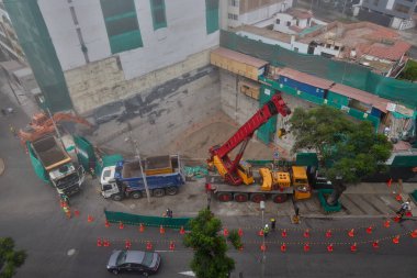 Bir vinç Miraflores, Lima 'daki kentsel bir inşaat sahasında, temel çalışması sırasında vinç operasyonları, güvenlik bariyerleri ve kontrollü lojistik faaliyetlerini gösteren bir inşaat malzemesi çıkarıyor. Sahne profesyonelliği vurguluyor.