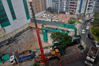 Bir vinç Miraflores, Lima 'daki kentsel bir inşaat sahasında, temel çalışması sırasında vinç operasyonları, güvenlik bariyerleri ve kontrollü lojistik faaliyetlerini gösteren bir inşaat malzemesi çıkarıyor. Sahne profesyonelliği vurguluyor.