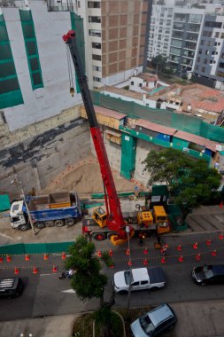 Bir vinç Miraflores, Lima 'daki kentsel bir inşaat sahasında, temel çalışması sırasında vinç operasyonları, güvenlik bariyerleri ve kontrollü lojistik faaliyetlerini gösteren bir inşaat malzemesi çıkarıyor. Sahne profesyonelliği vurguluyor.