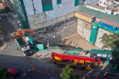 Bir vinç Miraflores, Lima 'daki kentsel bir inşaat sahasında, temel çalışması sırasında vinç operasyonları, güvenlik bariyerleri ve kontrollü lojistik faaliyetlerini gösteren bir inşaat malzemesi çıkarıyor. Sahne profesyonelliği vurguluyor.