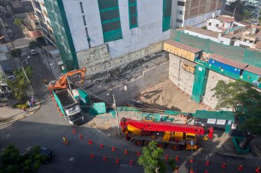 Bir vinç Miraflores, Lima 'daki kentsel bir inşaat sahasında, temel çalışması sırasında vinç operasyonları, güvenlik bariyerleri ve kontrollü lojistik faaliyetlerini gösteren bir inşaat malzemesi çıkarıyor. Sahne profesyonelliği vurguluyor.