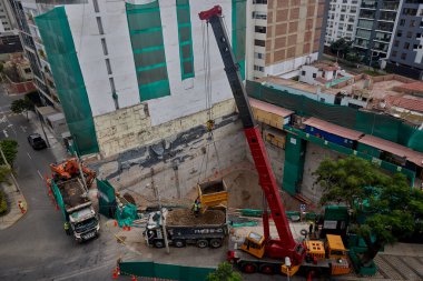 Bir vinç Miraflores, Lima 'daki kentsel bir inşaat sahasında, temel çalışması sırasında vinç operasyonları, güvenlik bariyerleri ve kontrollü lojistik faaliyetlerini gösteren bir inşaat malzemesi çıkarıyor. Sahne profesyonelliği vurguluyor.