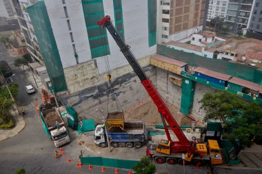 Bir vinç Miraflores, Lima 'daki kentsel bir inşaat sahasında, temel çalışması sırasında vinç operasyonları, güvenlik bariyerleri ve kontrollü lojistik faaliyetlerini gösteren bir inşaat malzemesi çıkarıyor. Sahne profesyonelliği vurguluyor.