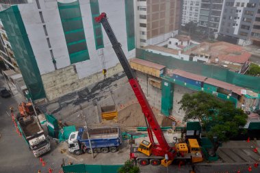 Bir vinç Miraflores, Lima 'daki kentsel bir inşaat sahasında, temel çalışması sırasında vinç operasyonları, güvenlik bariyerleri ve kontrollü lojistik faaliyetlerini gösteren bir inşaat malzemesi çıkarıyor. Sahne profesyonelliği vurguluyor.
