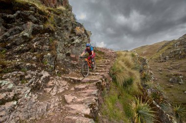 Peru, Cusco 'da antik dağlık patikalar boyunca seyahat eden bir grup dağ bisikletçisi, otantik yerel kültür, tarihi manzaralar ve uzak bir And ortamında aktif bir yaşam tarzı ve keşif ruhunu yansıtan açık hava maceraları yaşıyorlar..