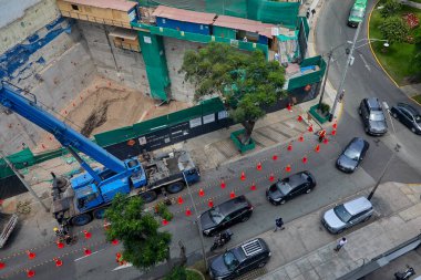 İşçiler şehir ortamında iyi uygulamalar ve yüksek çalışma standartlarını koordine ederek yerleşik güvenlik protokollerini uygularken, işaretli güvenlik konileri oluşturan kalabalık bir şehir şantiyesinin genel bakış açısı.