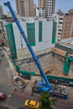 İşçiler şehir ortamında iyi uygulamalar ve yüksek çalışma standartlarını koordine ederek yerleşik güvenlik protokollerini uygularken, işaretli güvenlik konileri oluşturan kalabalık bir şehir şantiyesinin genel bakış açısı.