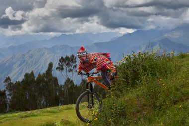 Peru And Dağları 'nın görkemli arka planına karşı, bir Chinchero çocuğu modern bir dağ bisikleti üzerinde ustalıkla engebeli bir yolda ilerliyor. Canlı, el yapımı bir panço ve geleneksel bir chullo giymişti.,