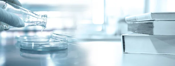 Bilim adamlarının elinde petri kabıyla matara ve araştırma laboratuarının arka planında bir yığın kitap var.