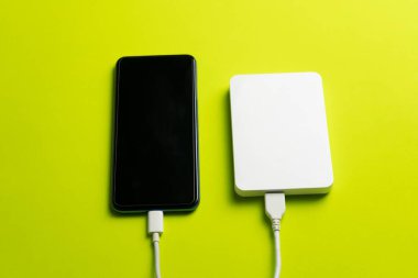 Yeşil arka plandaki harici sabit diske bağlanan akıllı telefon. Teknoloji, mobil veri depolama kavramı..