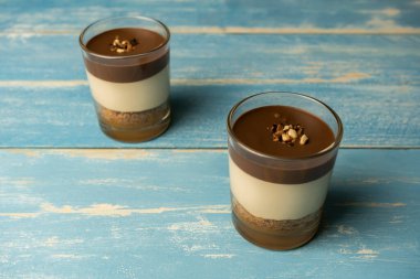 Bardakta iki çikolatalı tatlı (yoğurt ya da krema, kurabiye ve fındık) Mavi yaz ahşap arka planında şekerleme konsepti.