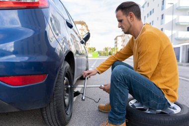 Genç adam vidaları ingiliz anahtarıyla söker. Kışı yaz lastikleri konseptine, patlak lastik tekerlek bakımına ve hizmet yaşam tarzına çevirir.