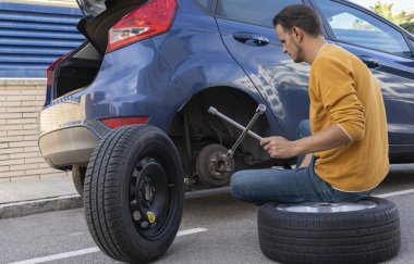 Genç adam tekerleği değiştirmek için ingiliz anahtarı kullanıyor..
