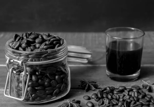 Black american coffee in glass with coffee beans in glass jar on rustic wooden table and dark background.