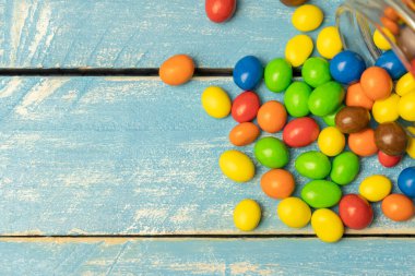 Cam kavanozdaki renkli çikolata topları mavi kırsal ahşap arka plana düştü..