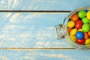 Mavi eski ahşap arka planda cam kavanozda çok renkli çikolata şekerlemeleri. Üst görünüm renkli tatlı arka plan konsepti. Metin için metin alanı ile fotokopi alanı.