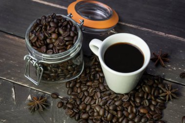 Cam kavanozda kahve çekirdekleri, Amerikan sade kahve fincanı ve eski ahşap masa. Kırsal arka planda yaratıcı kafe kavramı..