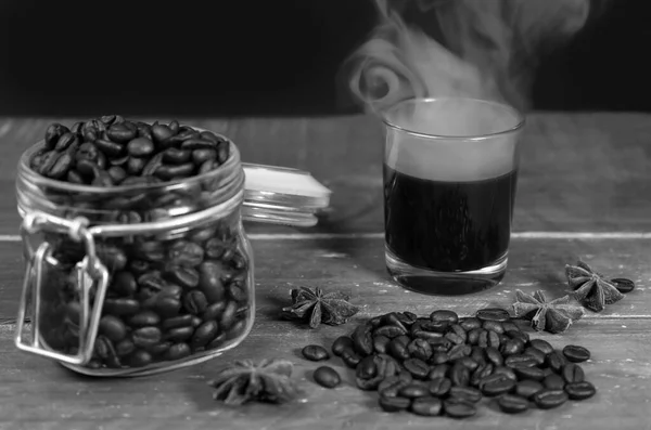 在玻璃杯里放热的黑咖啡和烟熏咖啡豆 在木制桌子上放罐 — 图库照片
