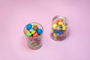 Pembe arka planda iki bardakta çok renkli çikolata şekerlemeleri. Yaratıcı renkli tatlı arka plan kavramının yakın plan görüntüsü ve metin için metin alanı.