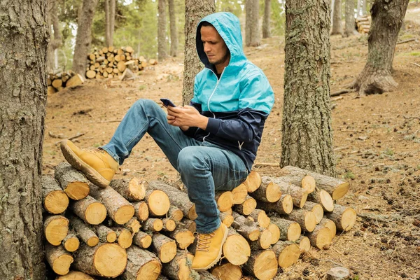 Man using smartphone sitting on a pile of wood logs in forest.Male using cell phone in nature,outdoor ,technology concept.