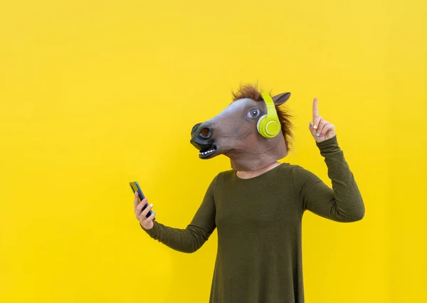Frau Mit Pferdekopfmaske Mit Smartphone Zeigt Mit Dem Finger Nach lizenzfreie Stockfotos