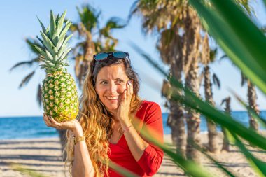 Mutlu kadın gün batımında palmiye yaprakları arasında ananas tutarken şaşırdı. Renkli sağlıklı meyve reklamcılığı kavramı..