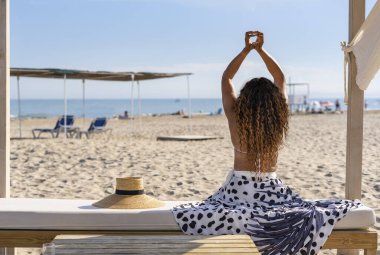 Tanımlanamayan kıvırcık saçlı, kolları havada ve elleriyle bir kalp yapan, plaj manzarasında bir bankta oturan güzel bir kadın..