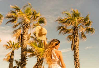 Arka planda plaj palmiyelerinde güneş şapkası tutan güzel bir kadın portresi. Yaz tatilleri konsepti yaşam tarzı.