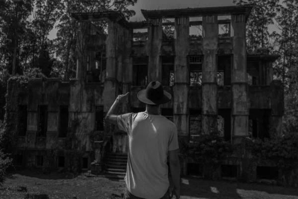 头戴牛仔帽的男子倒影指向恐怖的废弃房屋 — 图库照片