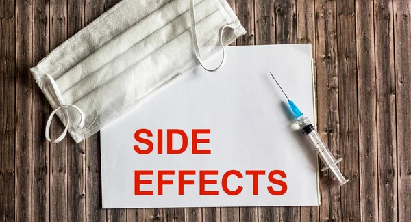 Side effect word on notepad with medical mask and vaccine on wooden table