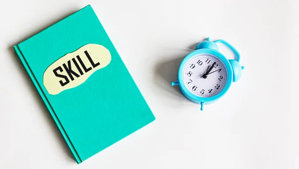The word SKILL is written on a notepad that lies on a white background, next to an alarm clock.