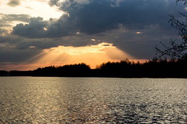Suyun üstünde renkli bir günbatımı. Güneş ışığı bulutların arasından doğar..