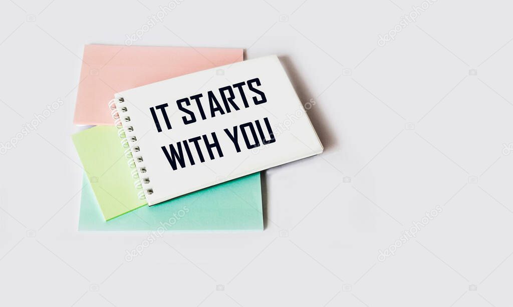 It all starts with you Motivational text is written on a notebook, next to stickers on a white background. Place to write