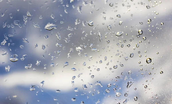 Raindrops on the window pane, blue sky and clouds visible through the transparent glass of the window