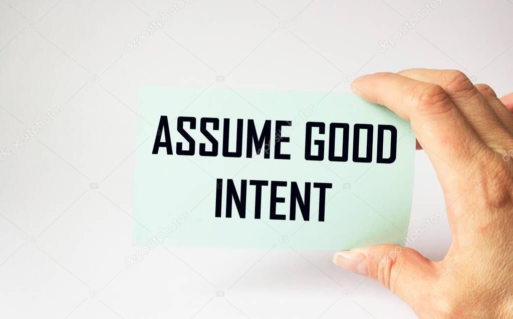 Assume good intent, card is held by female hand on white background. Good intentions on sticker, positive and personal development concept