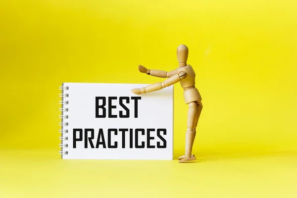 Best practices, the text is written on a notebook, next to a wooden doll on a yellow background. Positive quote.