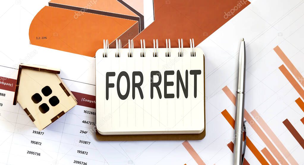 FOR RENT text on the notepad with paper sheet with pen and wooden house