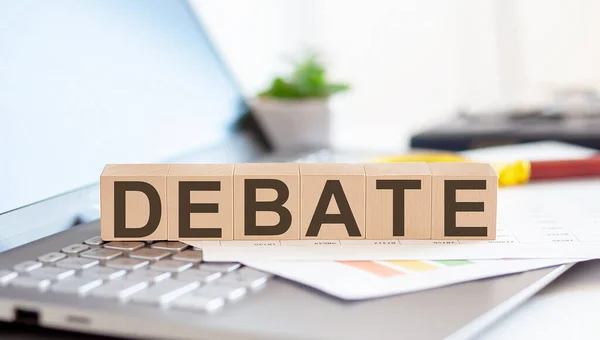 DEBATE Wooden cubes with letters on a laptop keyboard with charts , magnifier