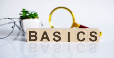 Tahta küpler ve çiçek, bardaklar, madeni paralar ve beyaz arka planda büyüteç üzerine BASICS kavramı