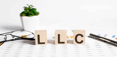 LLC kelime kavramı ahşap bloklara yazılmış, küpler çiçek, kalem ve bardaklar arkaplanda