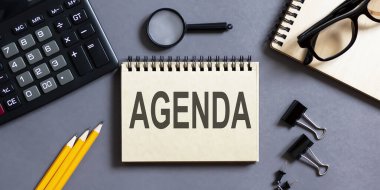 Üzerinde AGENDA yazıları olan gri bir arkaplan ve ofis aletleri olan bir not. iş